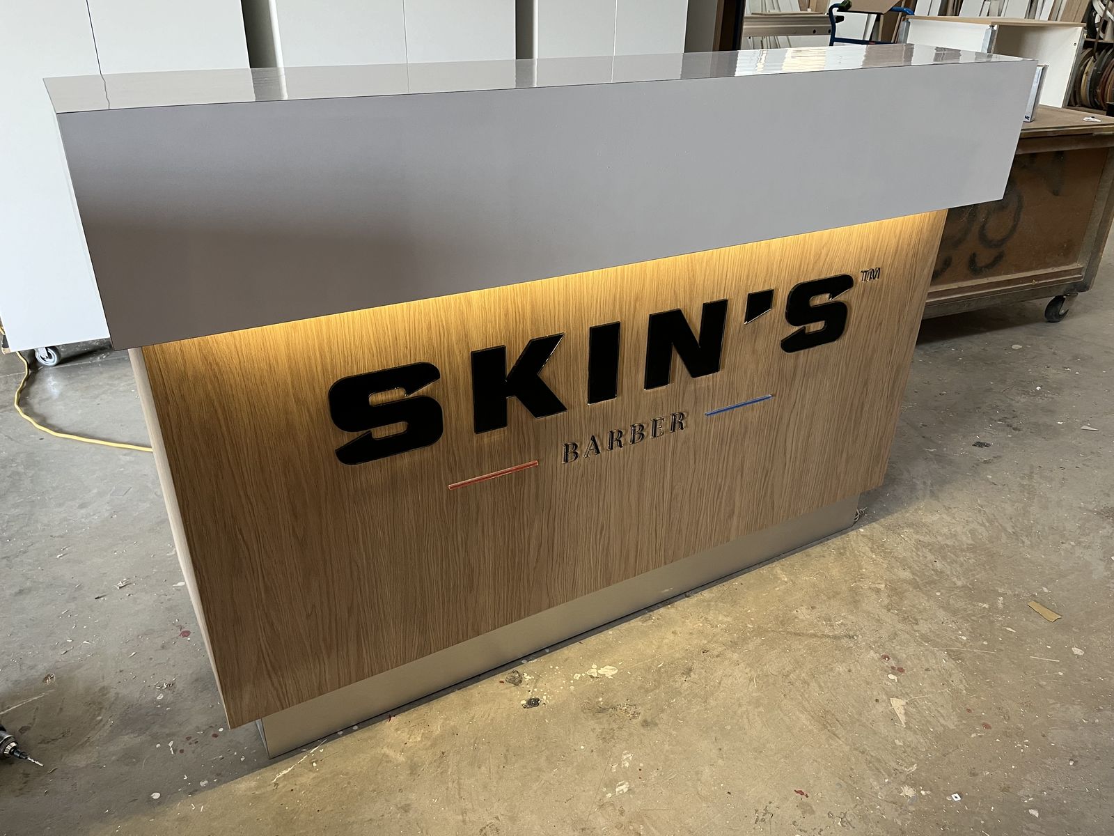 Illuminated timber reception desk with 'Skin's' barber signage
