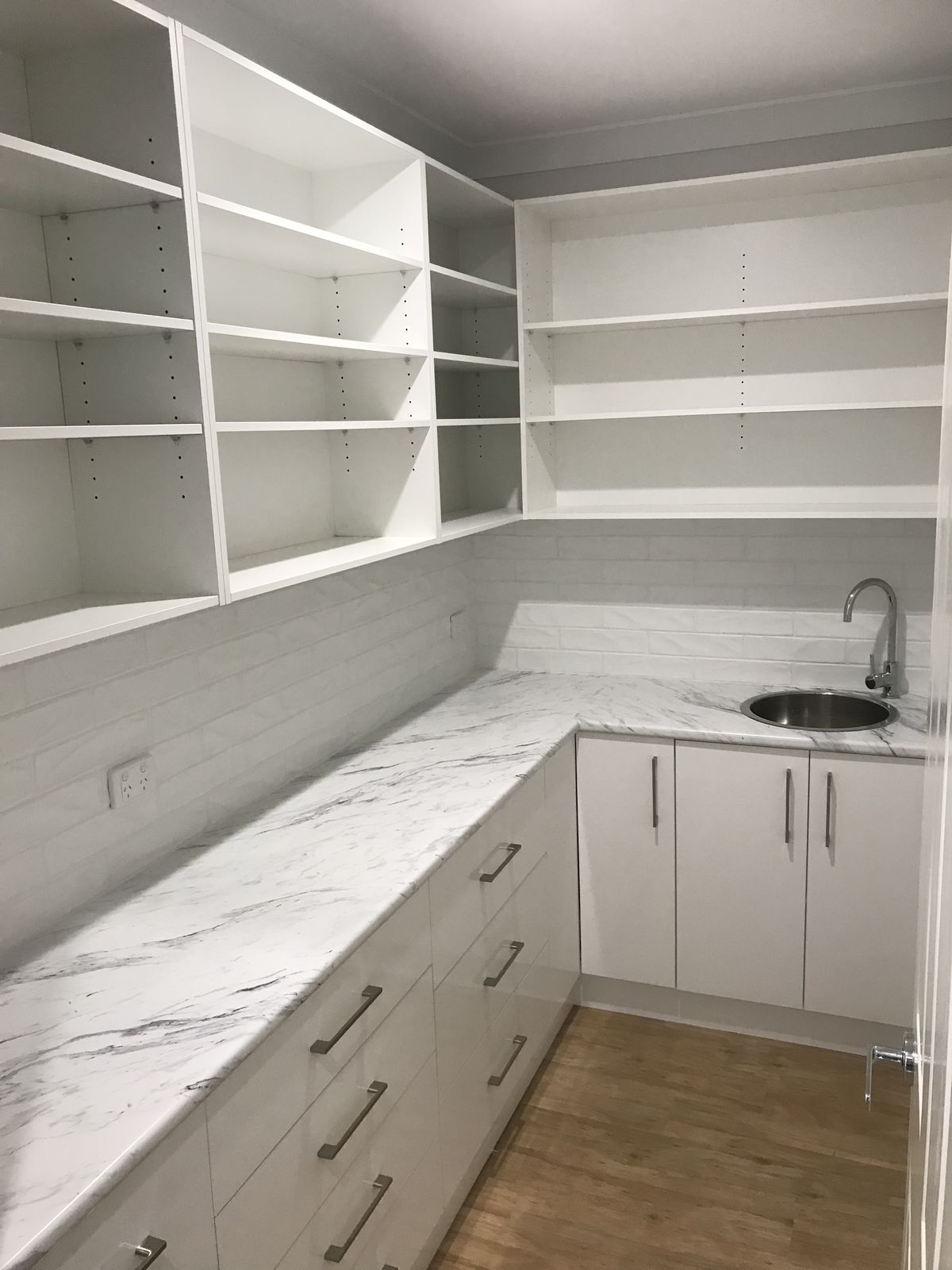 Walk-in butler's pantry with white cabinetry, stone bench and marble splashback