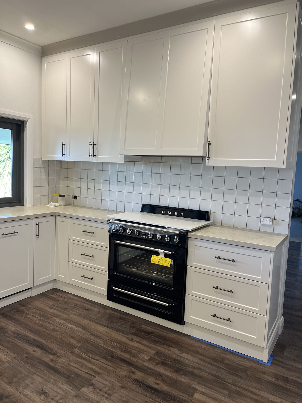 White kitchen with a black freestanding oven and timber-look flooring