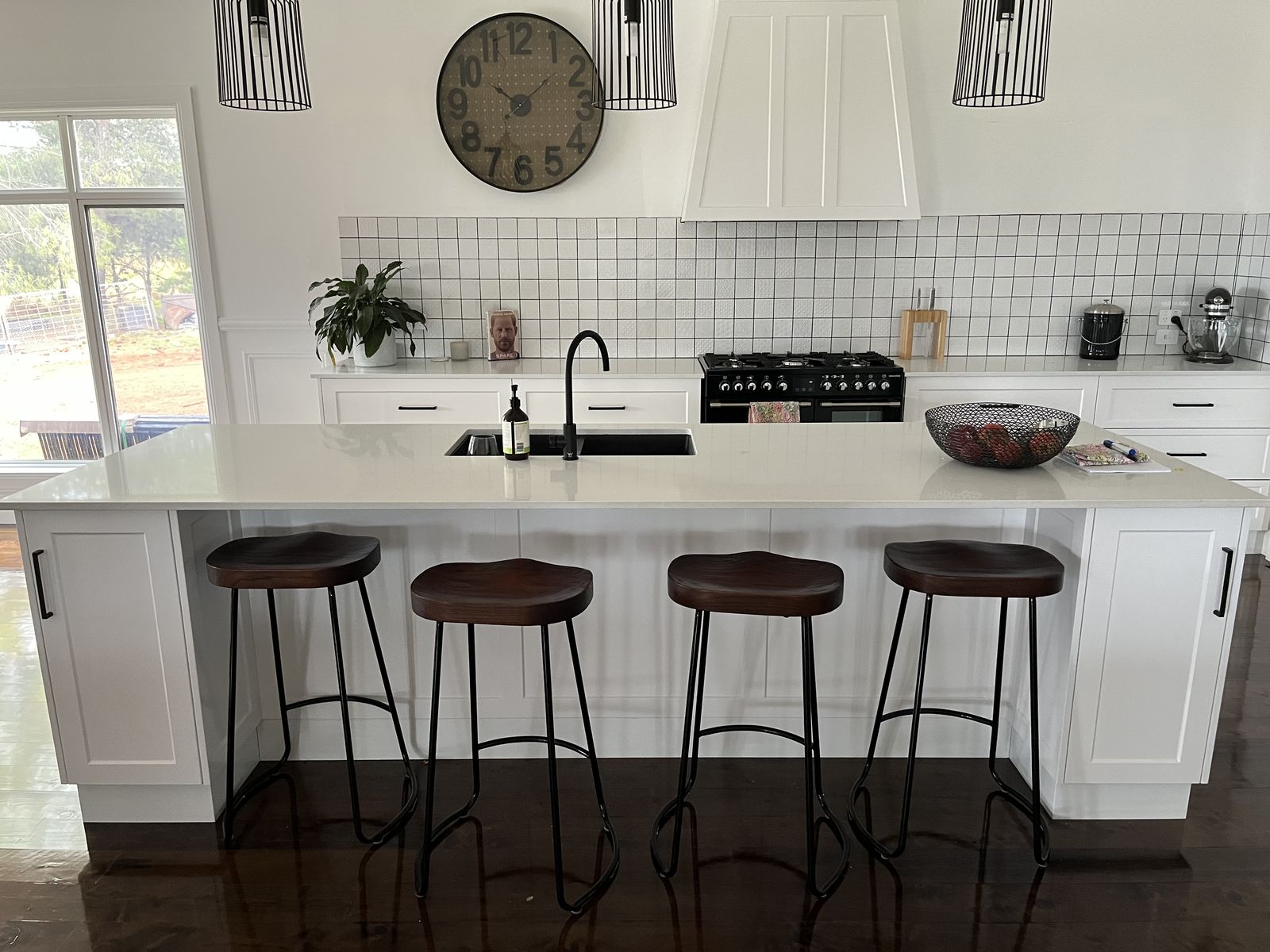 White shaker island kitchen with black stools and pendant lighting