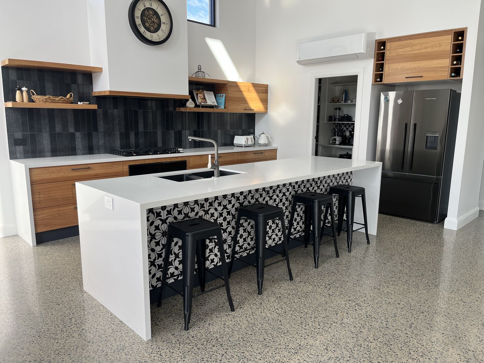 Full view of a custom white kitchen with island, timber shelves and dark splashback