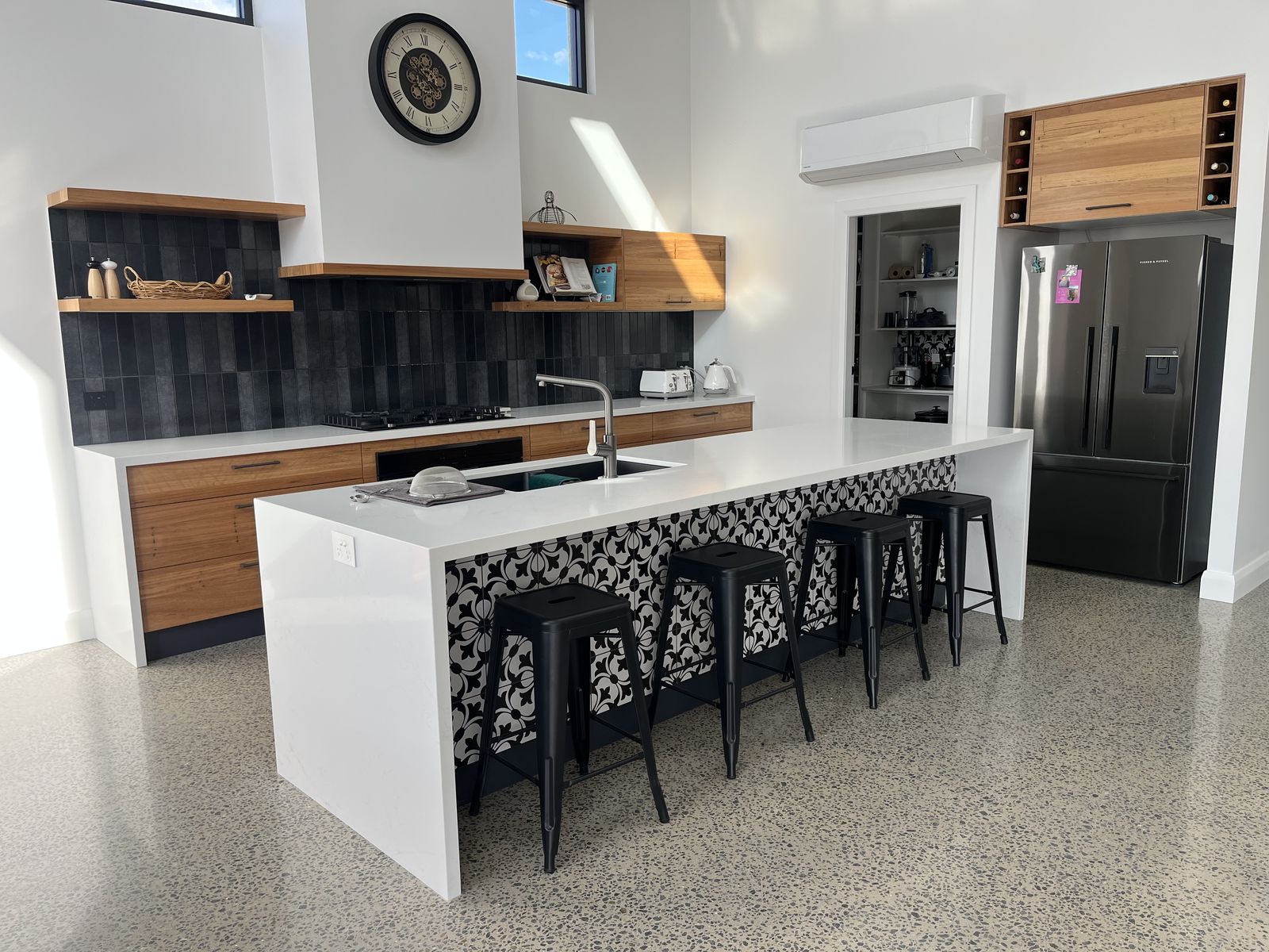 Custom white shaker kitchen with large stone island, patterned splashback and black bar stools