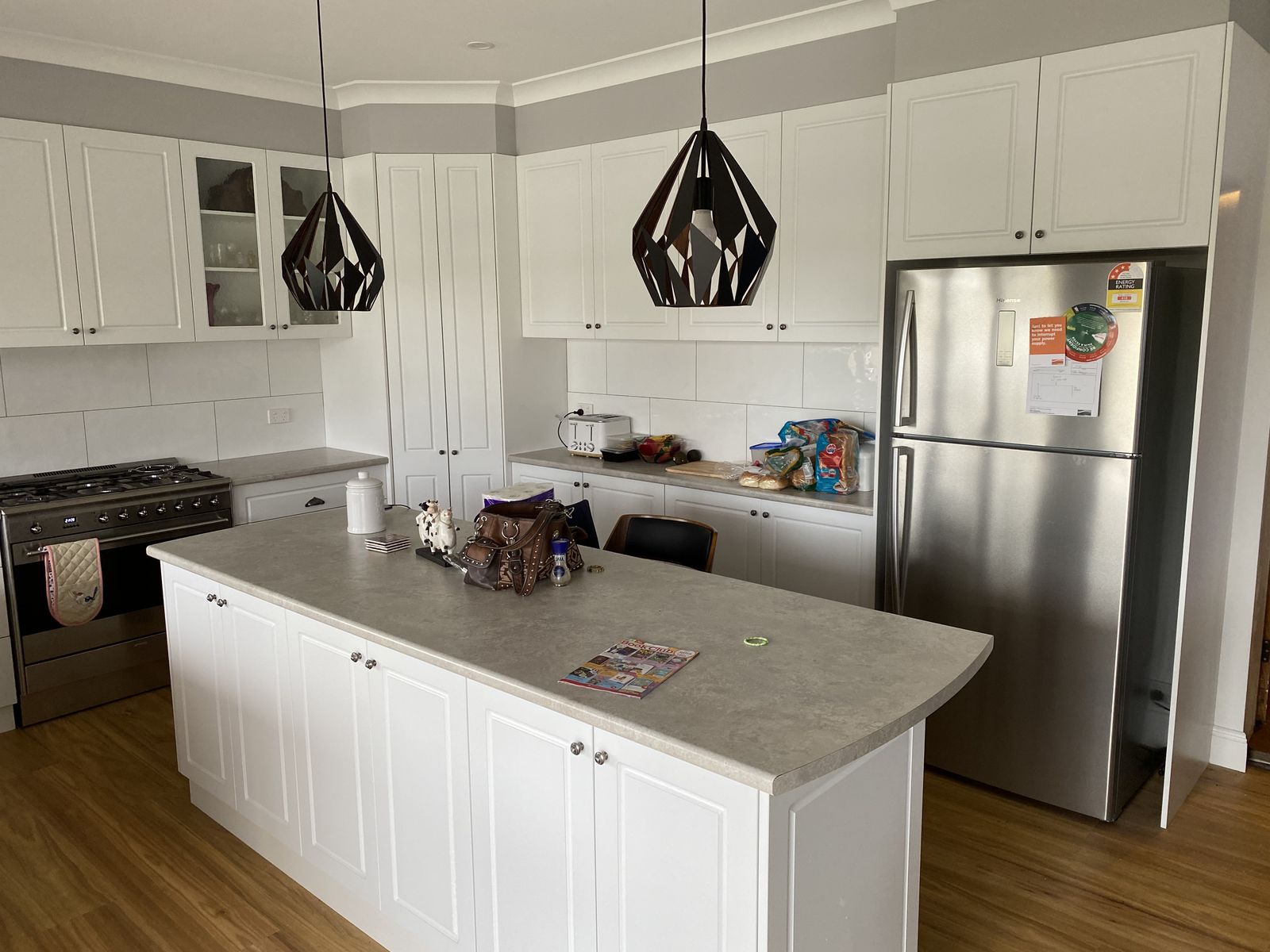 White kitchen with black pendant lights, stone island and stainless appliances