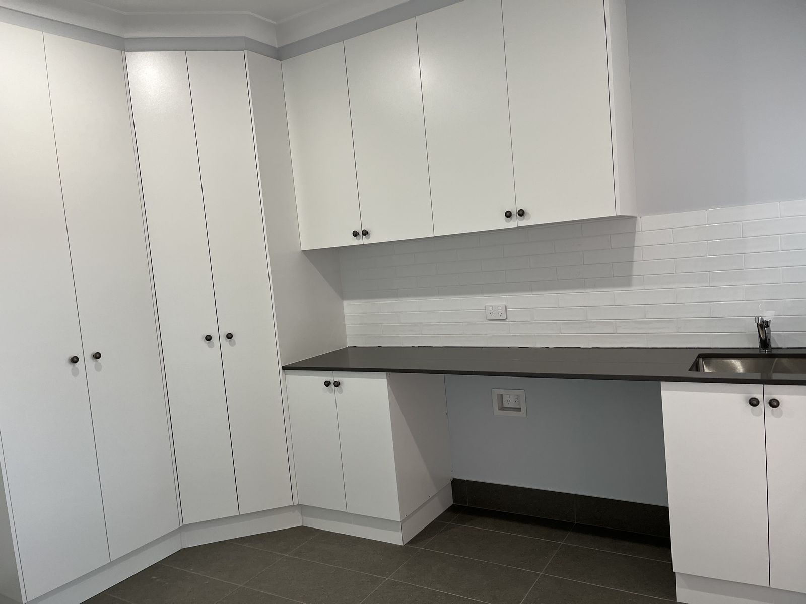 White laundry with overhead cabinets, stone benchtop and built-in desk nook