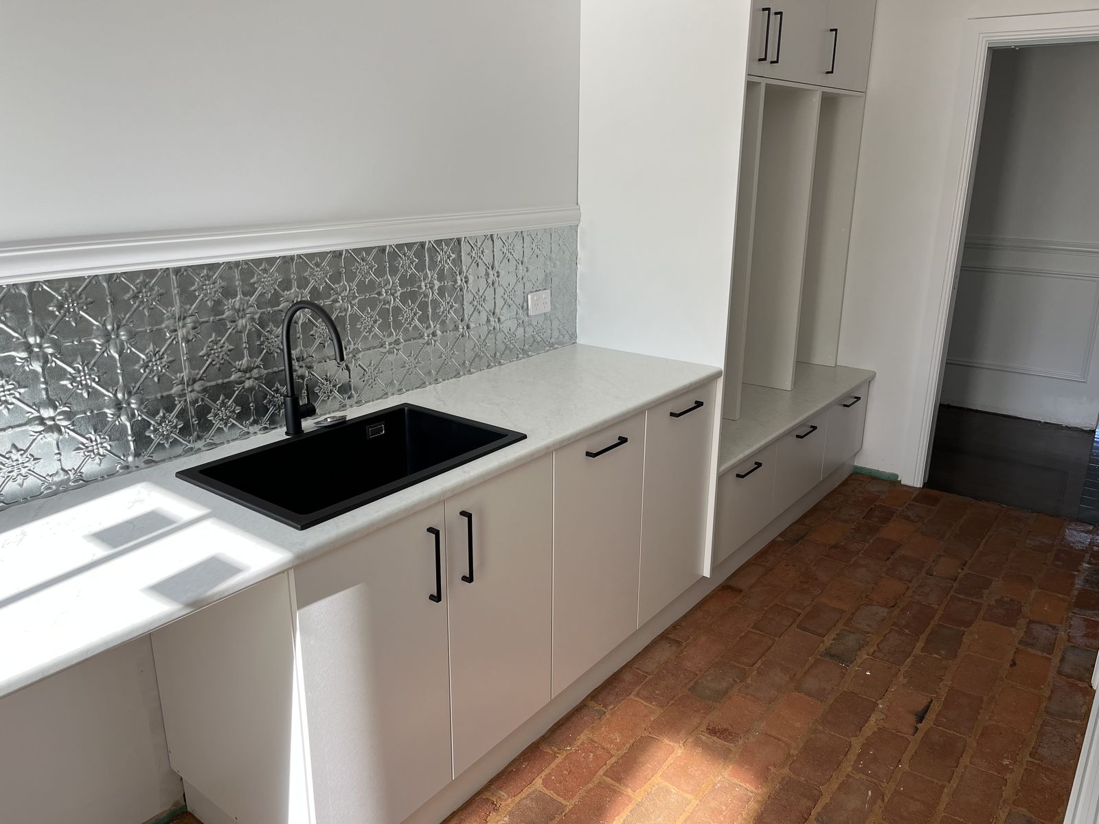 Laundry with pressed-metal splashback, black sink and white cabinetry