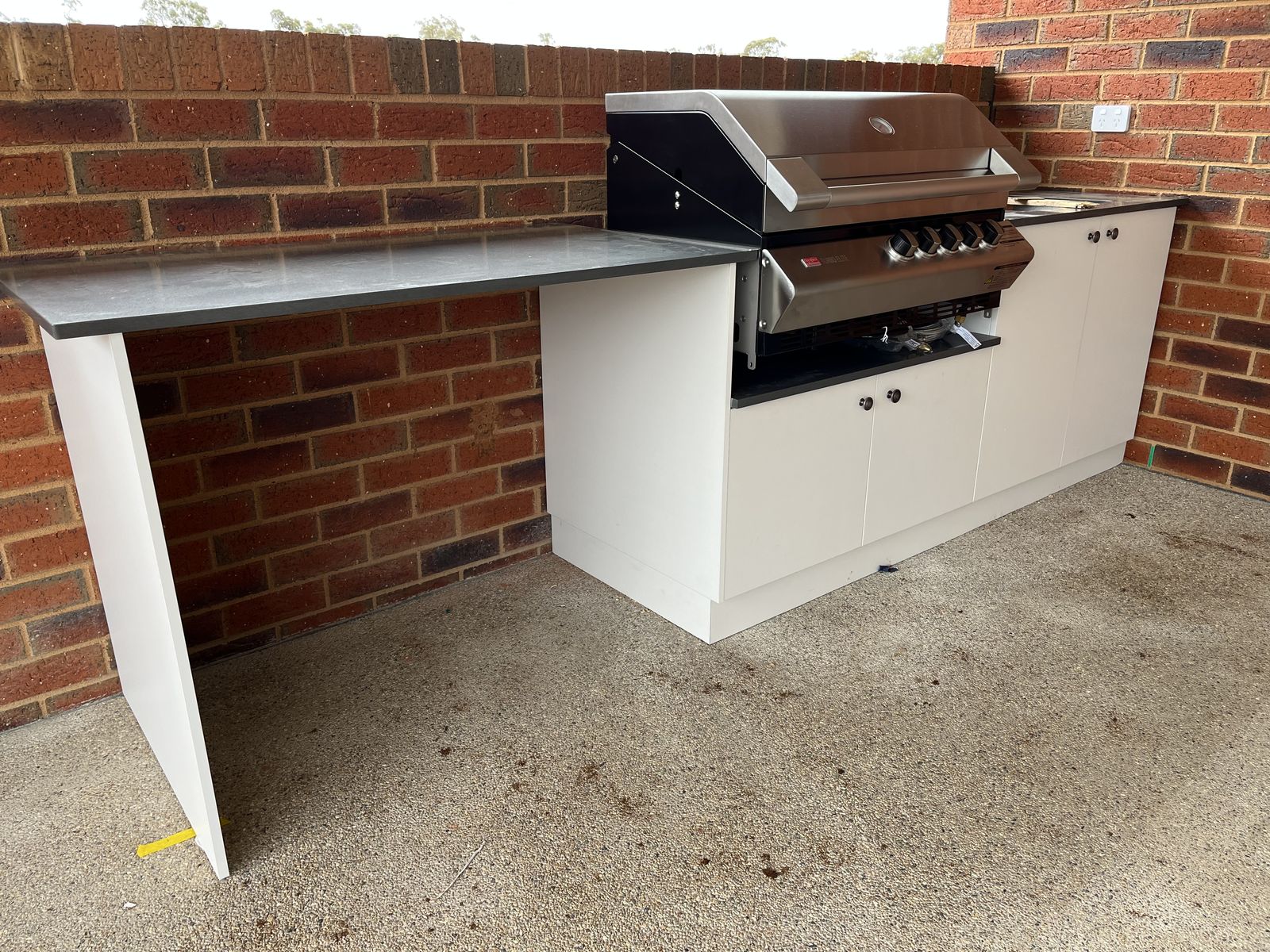 Alfresco BBQ area with white cabinetry and stone benchtop against brick