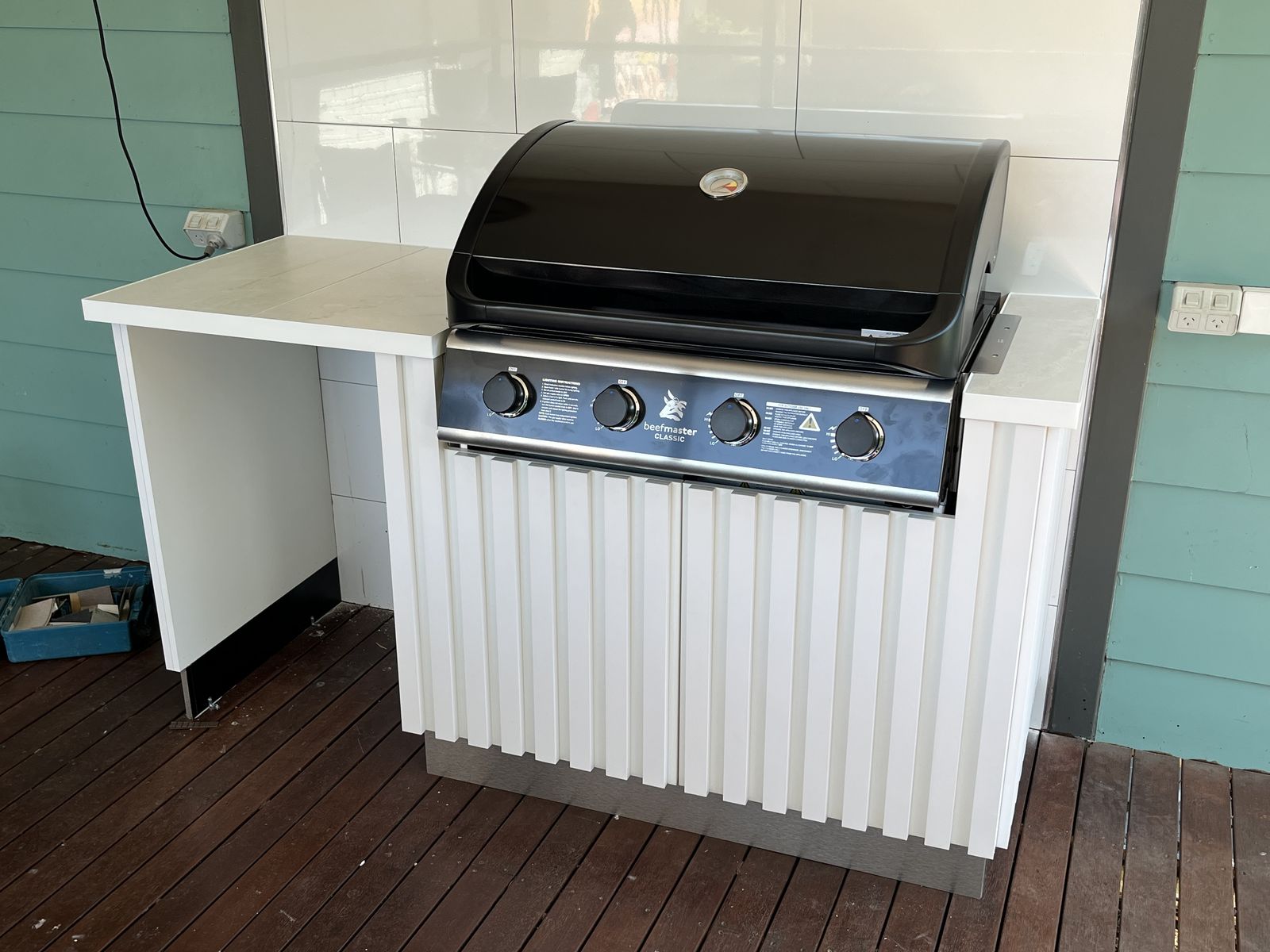 Outdoor barbecue island with fluted white cabinetry on a timber deck
