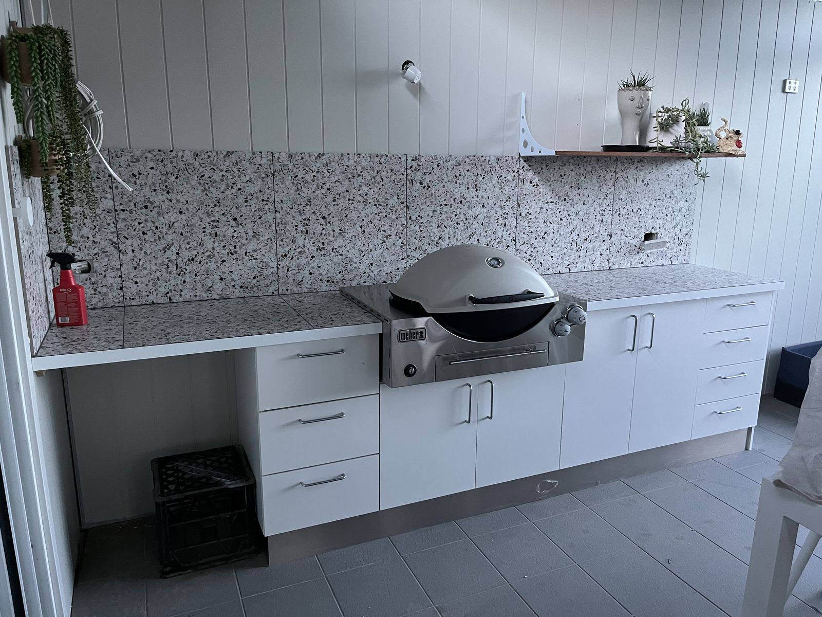 Outdoor kitchen with built-in BBQ, stone benchtop and white cabinetry
