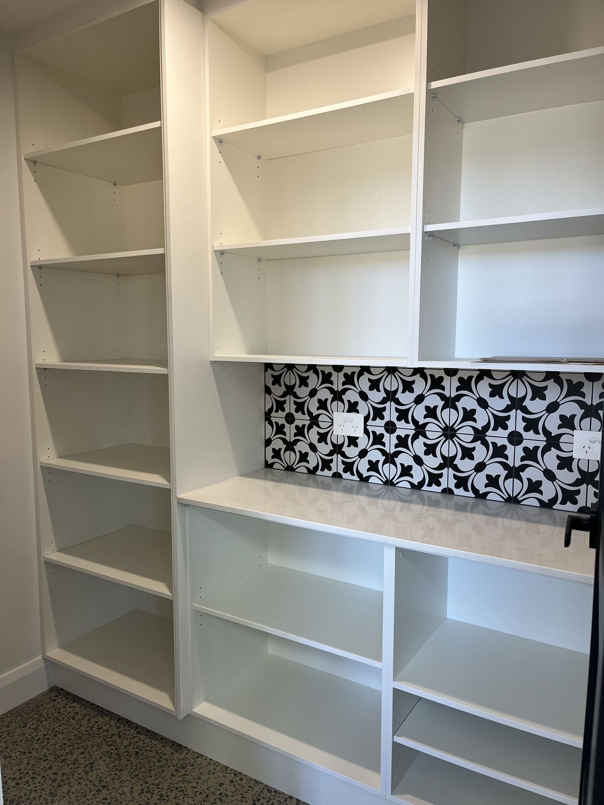 Freestanding white pantry and shelving unit with black-and-white tile detail