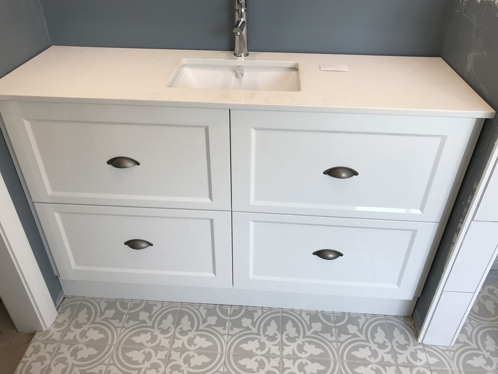 White shaker vanity with stone top over a patterned tiled floor