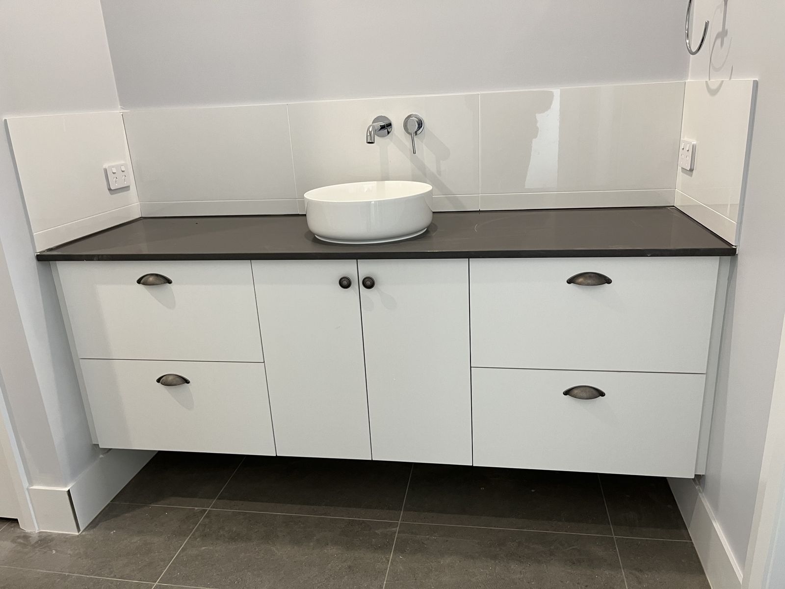White vanity with dark stone benchtop, vessel basin and grey mosaic splashback